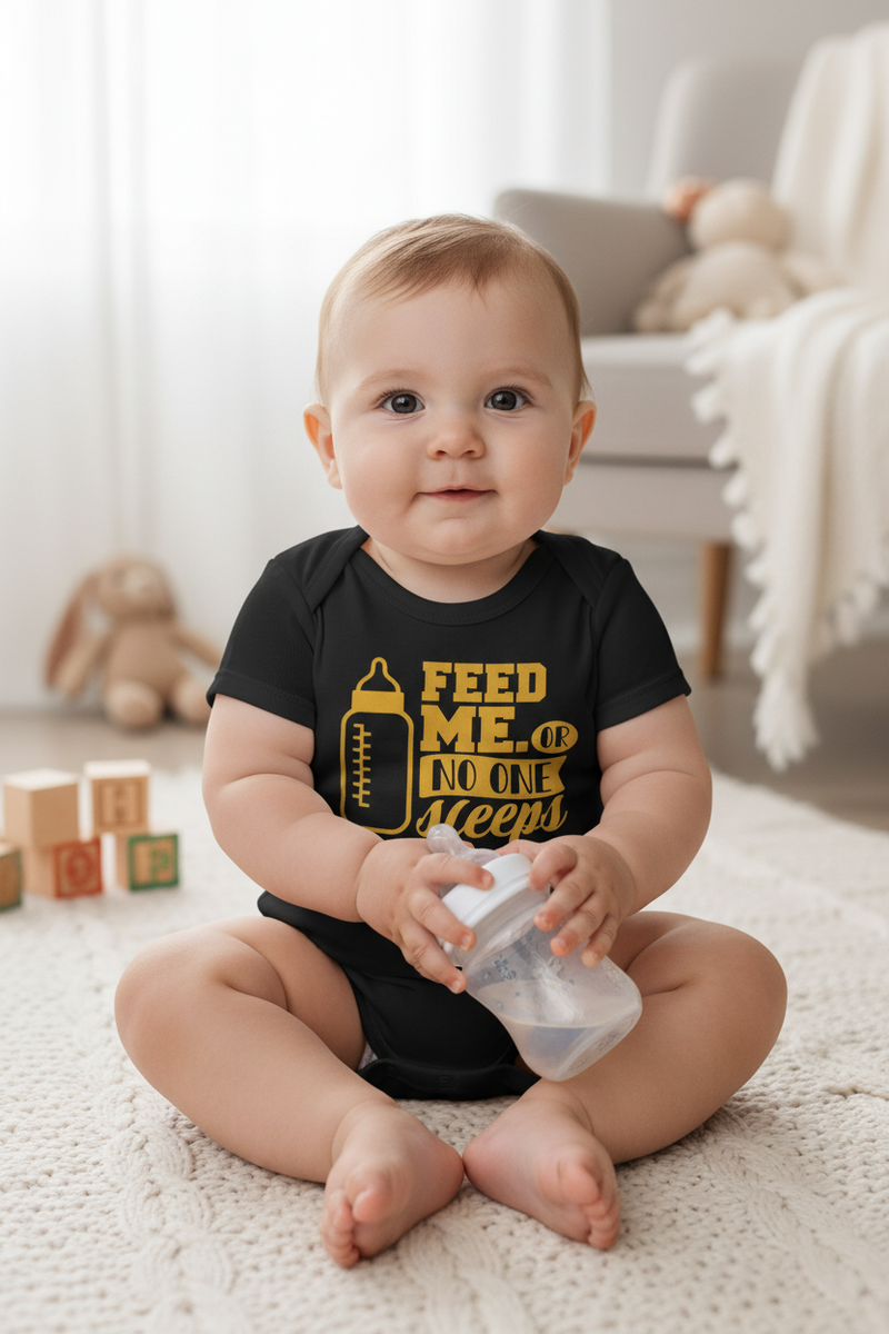 Baby sitting on a carpeted floor holding a bottle, wearing a black onesie with yellow text.