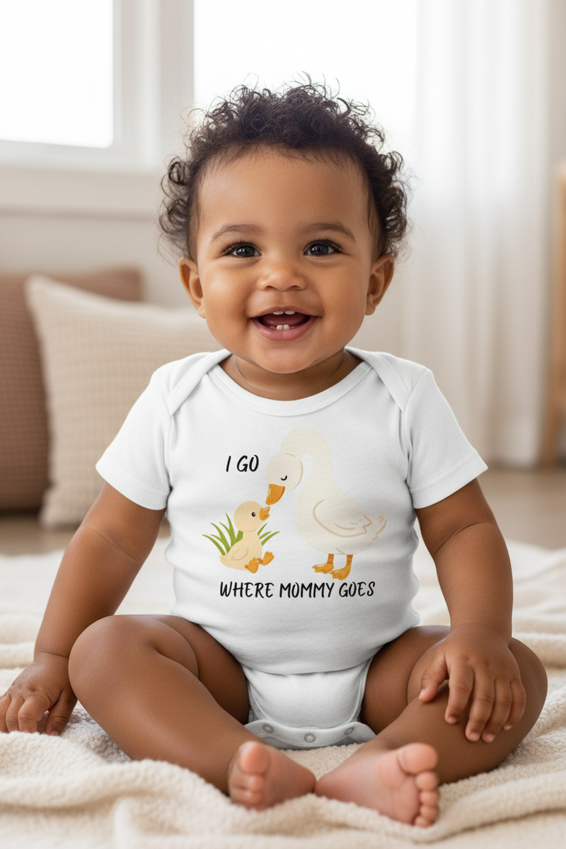 Baby wearing a onesie with a duck design and text, sitting on a blanket.