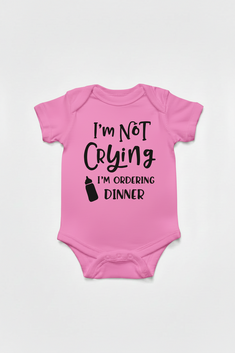 Pink baby onesie with text 'I'm Not Crying, I'm Ordering Dinner' on a white background
