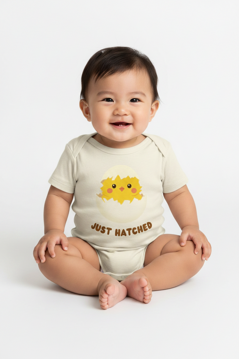 Baby wearing a onesie with a sun design and 'Just Hatched' text on a white background